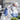 Person in a lab coat and protective gear holding a test tube with plants in the background